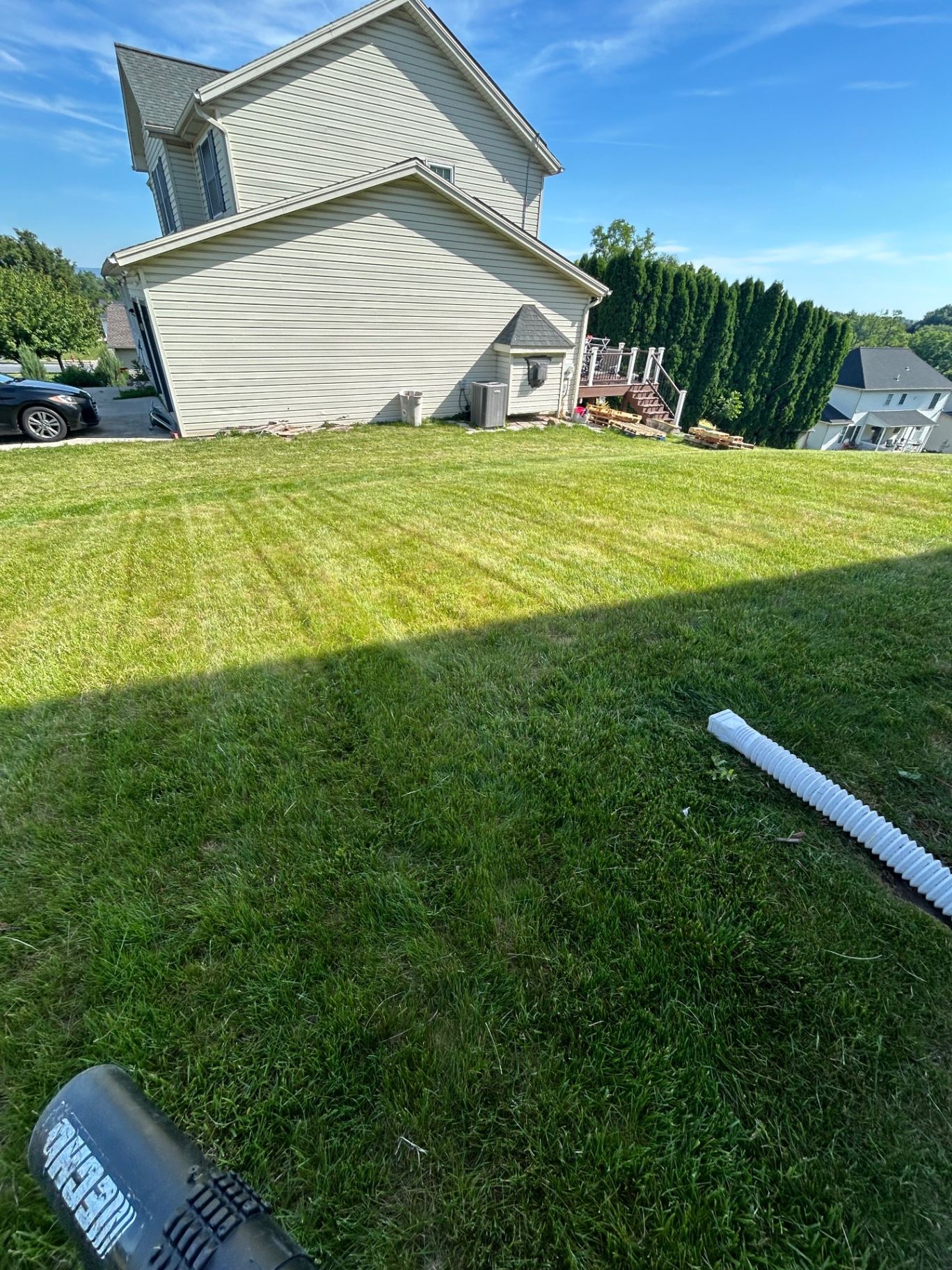 Sloped backyard lawn with fresh mowing lines beside a home and deck stairs